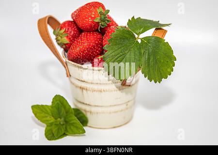 Frische Erdbeeren mit Minzblättern im dekorativen weißen Eimer, isoliert auf weißem Hintergrund Stockfoto