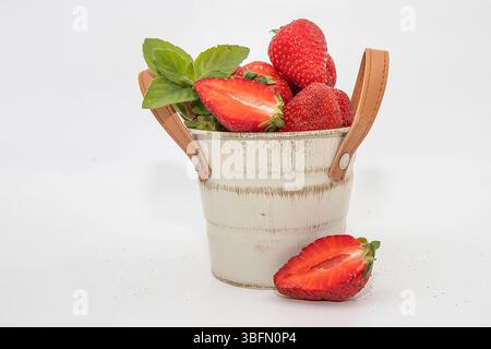Frische Erdbeeren mit Minzblättern im dekorativen weißen Eimer, isoliert auf weißem Hintergrund Stockfoto