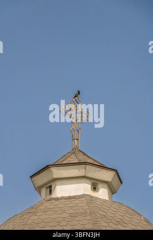 Am späten Nachmittag steht ein Vogel auf einem metallischen Kreuz auf dem Dach einer kleinen Kapelle. Die Kapelle ist Teil der Sacred Heart Church und hat sie auch Stockfoto
