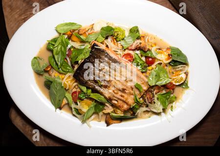 Ein Lachsfilet wird mit Gemüse und Kräutern überzogen, wodurch ein ansprechendes Gericht zum Servieren entsteht. Stockfoto