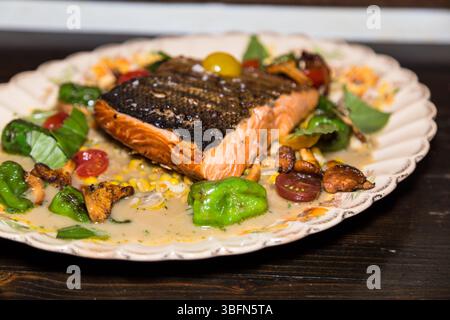 Ein Lachsfilet wird mit Gemüse und Pilzen auf einem dekorativen Teller serviert und bietet eine gesunde und köstliche Mahlzeit. Stockfoto