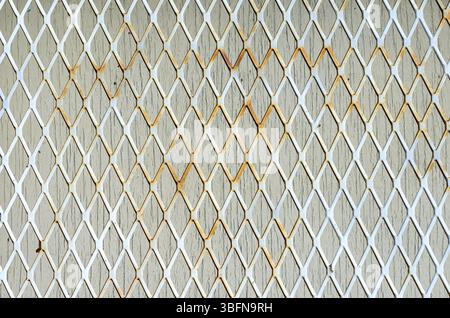 Nahaufnahme von weißem rostigem Metallgitter über hölzernem Fenstereinsatz. Stockfoto