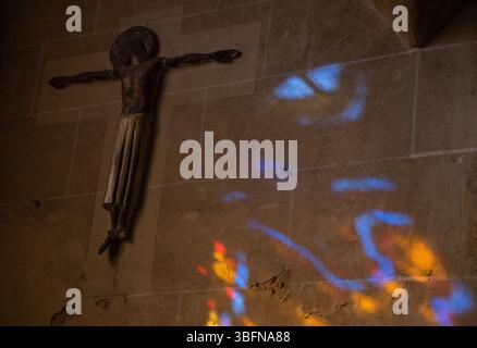 Buntes Licht filtert durch Buntglasfenster in der alten Kapelle und schafft mystische spirituelle abstrakte Kunst an einer Steinmauer in der Nähe eines antiken hölzernen Kruzifix Stockfoto