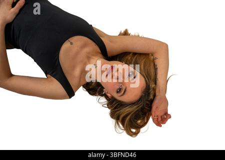 Studio-Aufnahme einer attraktiven jungen Frau mit Tätowierungen, die in einem schwarzen Tanktop liegt Stockfoto