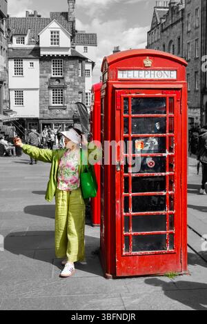 asiatische Touristin in bunten Outfit, die ein Selfie neben einer klassischen roten britischen Telefonbox Royal Mile edinburgh schwarz-weiß Hintergrund macht Stockfoto