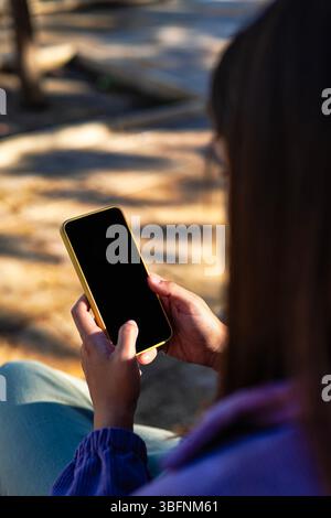 Rückansicht einer Frau mit Handy in der Hand, schwarzer Bildschirm, verschwommener urbaner Hintergrund, minimalistischer Stil mit viel Kopierraum. Stockfoto