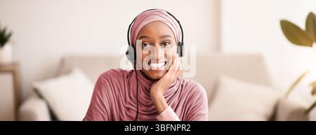 Portrait der schönen muslimischen schwarzen Frau im Kopftuch trägt Headset, online kommunizieren auf Laptop-Computer, drinnen Stockfoto