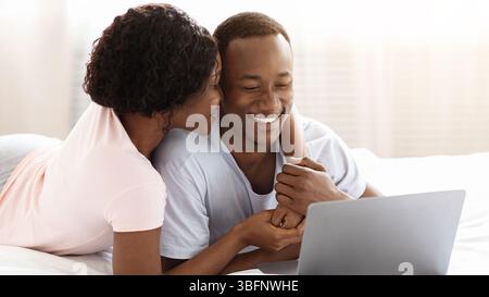 Romantischer schwarzer Mann und Frau mit Laptop im Bett Stockfoto