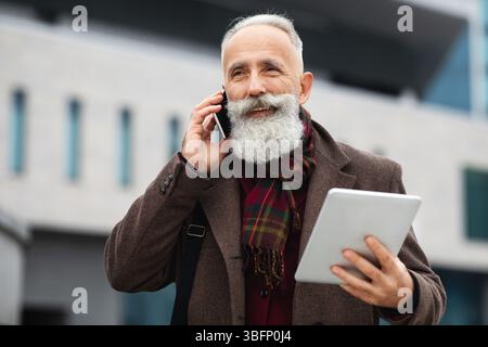 Schöner grauhaariger Mann, der am Telefon telefoniert, während er auf der Straße unterwegs ist Stockfoto