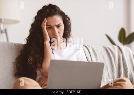Aufgewühlte junge Frau sitzt auf der Couch mit Laptop, Nahaufnahme Stockfoto