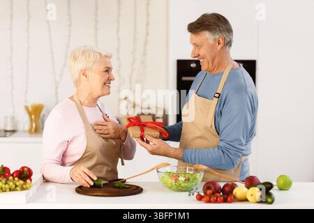 Älterer Mann Schenkt Der In Der Küche Stehenden Ehefrau Ein Geburtstagsgeschenk Stockfoto