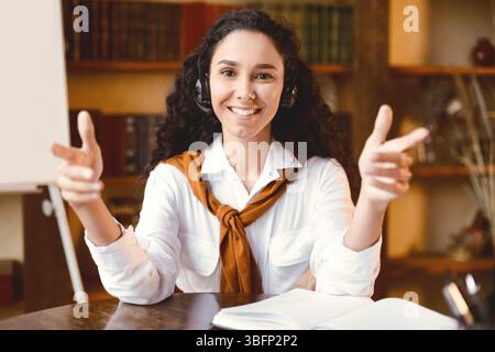 Frau, die am Schreibtisch sitzt und mit der Kamera spricht, die ein Headset trägt Stockfoto
