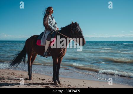 Junge asiatische Frau reitet am Sommertag auf einem Pferd am Seeufer Stockfoto