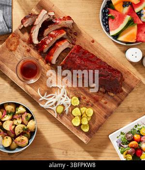 Grillrippchen mit Gurken, Zwiebeln, Salat, Kartoffeln und Obst Stockfoto
