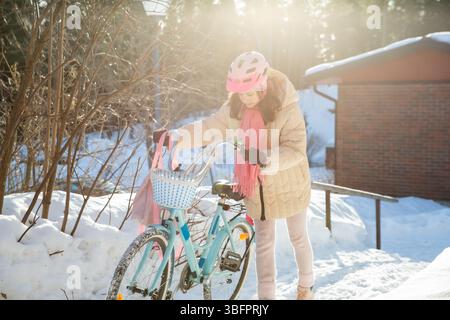 Tween geht mit ihrem Fahrrad nach Hause an einem sonnigen Wintertag in einem finnischen Vorort. Schnee auf dem Boden, ein echter Moment des nordischen Alltags. Stockfoto