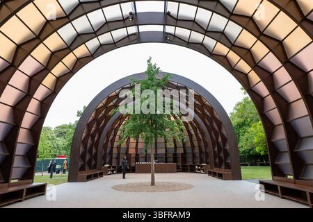 London, Großbritannien. Juni 2025. Der Serpentine Pavilion 2025, Eine Kapsel in Time, entworfen von der bangladeschischen Architektin und Pädagogin Marina Tabassum und ihrer Firma Marina Tabassum Architects (MTA), wird am 6. Juni 2025 eröffnet. Goldman Sachs unterstützt das jährliche Projekt zum 11. Jahr in Folge. Aus Holz gefertigt und um einen halbReifen Ginkgo-Baum gebaut (eine klimaresistente Baumart, die aus dem frühen Jura stammt) und eine Hälfte des Pavillons kann sich bewegen, um eine neue Konfiguration zu schaffen. Quelle: Mary-Lu Bakker/Alamy Live News Stockfoto