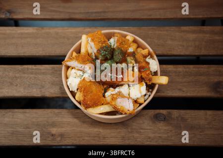 Poutine-Pommes mit Käse und gebratenem Huhn in einem Papierbehälter zum Mitnehmen. Köstliche frisch zubereitete Mahlzeit, perfekt für Menüs, Restaurants oder köstliche Speisen Stockfoto