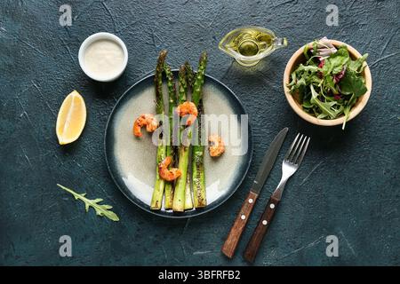 Teller mit gebratenem grünem Spargel und leckeren Garnelen auf dunklem Hintergrund Stockfoto