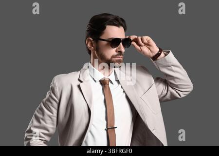 Hübscher junger Mann in hellem Anzug mit Sonnenbrille auf grauem Hintergrund Stockfoto