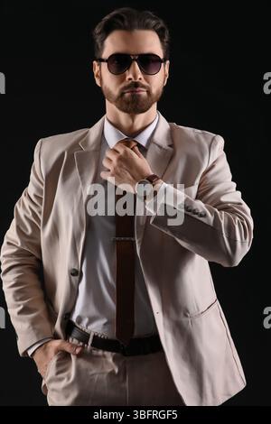Hübscher junger Mann in hellem Anzug mit Sonnenbrille auf schwarzem Hintergrund Stockfoto