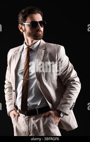 Hübscher junger Mann in hellem Anzug mit Sonnenbrille auf schwarzem Hintergrund Stockfoto