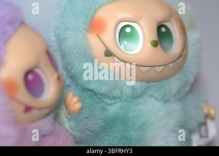 Zwei verspielte Labubu-Spielzeugfiguren in flauschigen grünen und rosa Monsterkostümen und einem schelmischen Lächeln, die vor weißem Hintergrund aufgestellt werden. Stockfoto