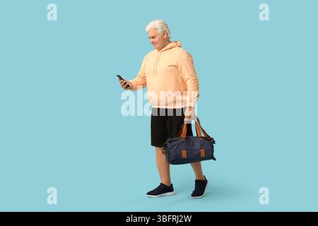Seniorenmann mit Sporttasche mit Handy auf blauem Hintergrund Stockfoto