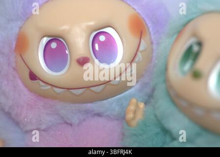 Zwei verspielte Labubu-Spielzeugfiguren in flauschigen grünen und rosa Monsterkostümen und einem schelmischen Lächeln, die vor weißem Hintergrund aufgestellt werden. Stockfoto