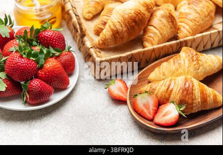 Frisch gebackene Croissants werden mit Erdbeeren und Honig serviert und sorgen so für ein köstliches Frühstück Stockfoto
