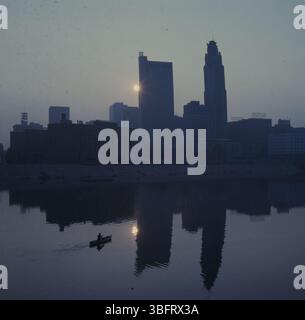 Ein Foto der Skyline von Columbus bei Sonnenaufgang, das den Scioto River mit einem Kanu zeigt. Die Gebäude der Stadt stehen vor dem frühen Morgenhimmel und schaffen eine ruhige, ruhige Szene. Stockfoto