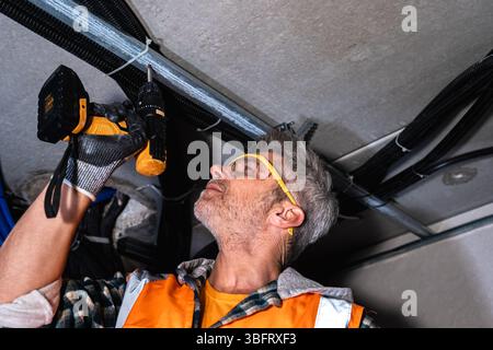 Professioneller Mitarbeiter, der mit einem Akku-Bohrer Metallrahmen an der Decke befestigt. Tragen von Handschuhen und Schutzbrille. Technische Konstruktion im Innenbereich Stockfoto