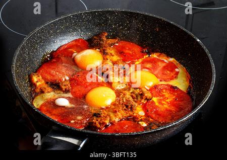 Spiegeleier mit Speck und Tomaten in einer Pfanne auf dem Herd Stockfoto