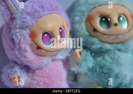Zwei verspielte Labubu-Spielzeugfiguren in flauschigen blau-rosa Monsterkostümen und einem schelmischen Lächeln vor weißem Hintergrund. Stockfoto