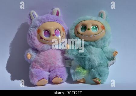 Zwei verspielte Labubu-Spielzeugfiguren in flauschigen blau-rosa Monsterkostümen und einem schelmischen Lächeln vor weißem Hintergrund. Stockfoto