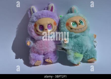 Zwei verspielte Labubu-Spielzeugfiguren in flauschigen blau-rosa Monsterkostümen und einem schelmischen Lächeln vor weißem Hintergrund. Stockfoto
