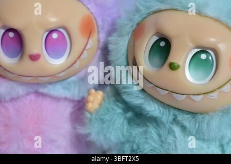 Zwei verspielte Labubu-Spielzeugfiguren in flauschigen blau-rosa Monsterkostümen und einem schelmischen Lächeln vor weißem Hintergrund. Stockfoto