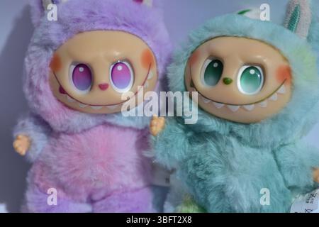Zwei verspielte Labubu-Spielzeugfiguren in flauschigen blau-rosa Monsterkostümen und einem schelmischen Lächeln vor weißem Hintergrund. Stockfoto