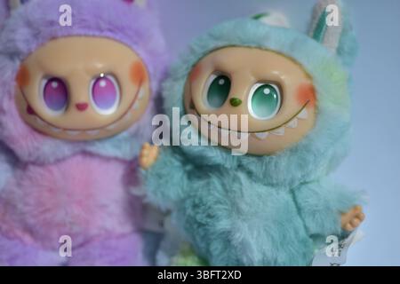 Zwei verspielte Labubu-Spielzeugfiguren in flauschigen blau-rosa Monsterkostümen und einem schelmischen Lächeln vor weißem Hintergrund. Stockfoto