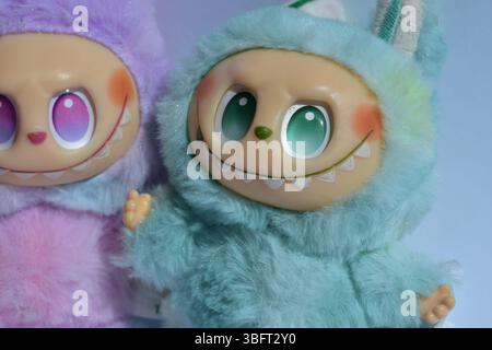 Zwei verspielte Labubu-Spielzeugfiguren in flauschigen blau-rosa Monsterkostümen und einem schelmischen Lächeln vor weißem Hintergrund. Stockfoto
