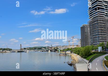 Krane und schwere Ausrüstung sind um das Gebäude herum sichtbar, mit der Belgrader Waterfront und der Skyline der Altstadt im Hintergrund. Wichtige Infrastruktur Stockfoto