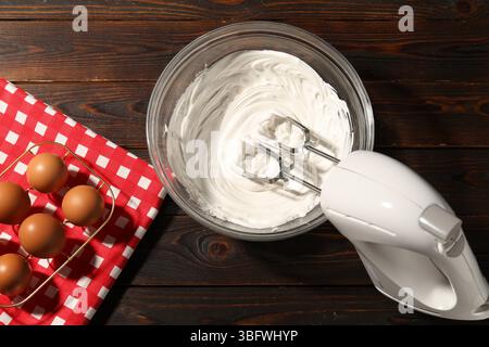 Handrührgerät, Schlagsahne in Schüssel und Eier auf Holztisch, flache Ladefläche Stockfoto