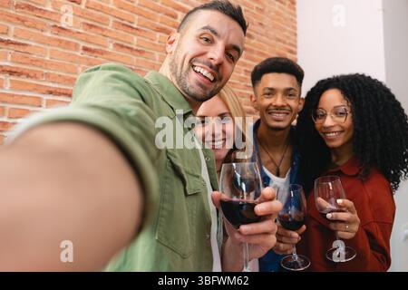 Gruppe von Freunden, die Selfie nehmen und während des Abendessens zu Hause mit Wein toasten Stockfoto