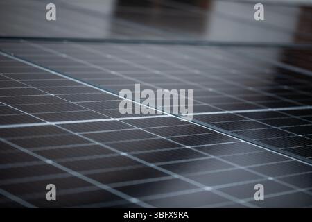 Leicht abgewinkelte Nahaufnahme von Solarpaneelen mit subtiler Reflexion des Nachbargebäudes, symbolisiert erneuerbare Energien und städtische Nachhaltigkeit Stockfoto