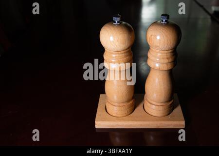 Hölzerne Salz- und Pfeffermühlen auf einem dunklen Holztisch schaffen eine rustikale und elegante Speise- oder Kücheneinrichtung. Stockfoto