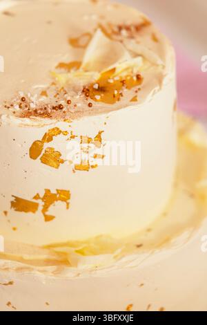 Cremiger zweistufiger Kuchen, dekoriert mit Blattgold, weißen Schokoladenspänen und Streuseln, perfekt für Feiern Stockfoto