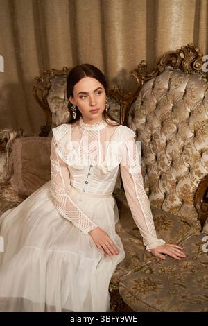 Eine wunderschöne junge Frau entspannt sich elegant in einem Vintage-Zimmer mit Plüschmöbeln. Stockfoto