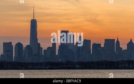 Die Skyline von Manhattan ist bei Sonnenaufgang mit warmen Orangetönen umrahmt und hebt das One World Trade Center über dem ruhigen Hudson River hervor. Stockfoto