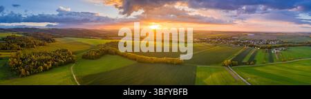 Hochauflösendes Weitwinkelpanorama der Drohne aus der Vogelperspektive über grüne Felder und Baumgruppen, Sonnenuntergang und schöne Wolken Stockfoto