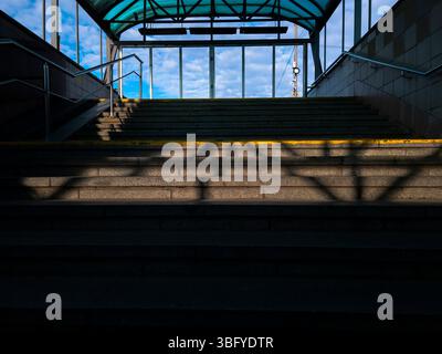 Leere Treppe, die zu einem hellblauen Himmel führt, in einer modernen Fußgängerzone mit Metallgeländern und transparentem Dach Stockfoto