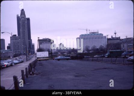 Dieser seltene Blick auf das Ohio Statehouse zeigt die östliche Seite, die von einem Parkplatz zwischen West Broad Street und Central High School auf der anderen Seite des Scioto River stammt. Der Blick fängt das leere Land zwischen Front Street und Statehouse ein, das auf den Bau wartet. Das Gebiet, das später zum Huntington Center entwickelt wurde, wurde während eines wirtschaftlichen Abschwungs vorübergehend geräumt, was zu Verzögerungen bei Projekten wie dem Vern Riffe Center for Government and the Arts führte. Stockfoto